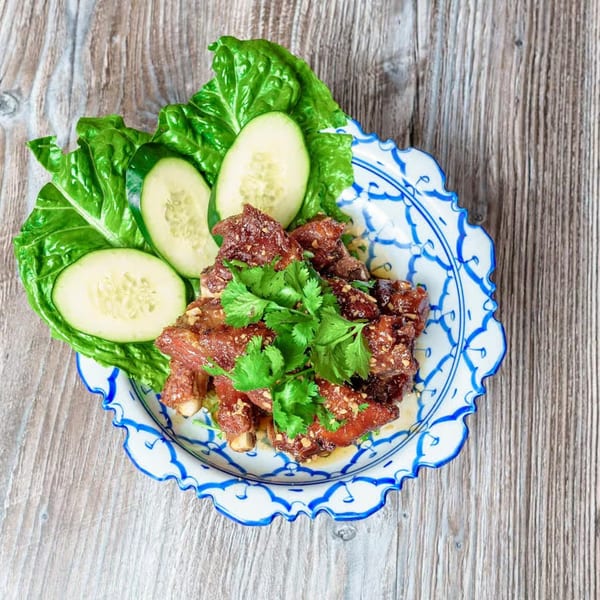 Thai E-San's crispy pork ribs with cilantro, lettuce, and cucumber slices on a decorative plate.