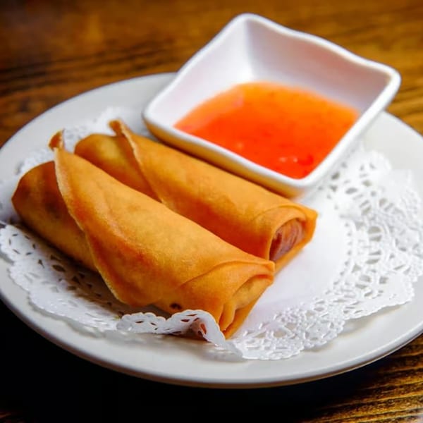 Three golden-brown Thai E-San spring rolls on a white plate with a side of sweet chili sauce.