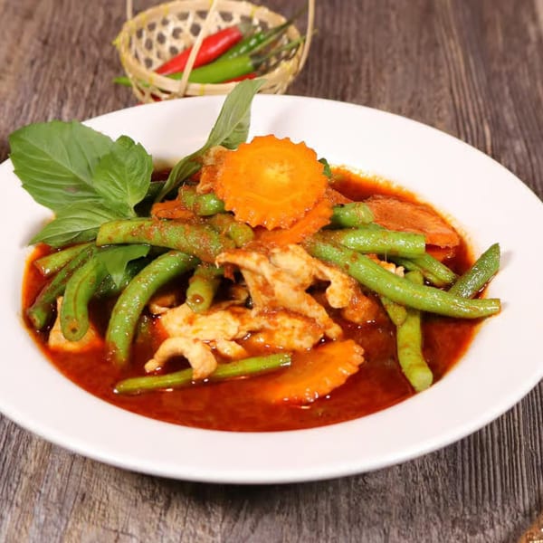 Thai E-San's red curry with chicken, green beans, carrots, and basil on a white plate.