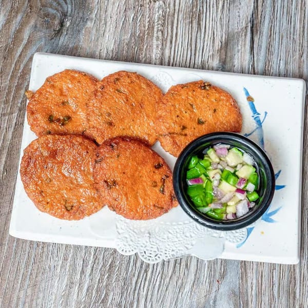 Five golden-brown Thai fish cakes with a side of cucumber relish on a white rectangular plate.