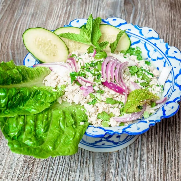 Thai Larb Gai with minced chicken, red onions, mint, and lettuce in a decorative bowl.