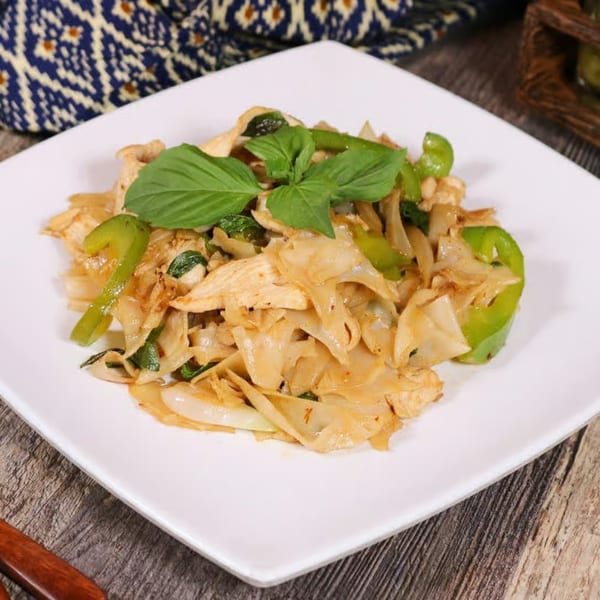 Thai E-San's Pad See Ew with wide noodles, chicken, green bell peppers, and basil on a white plate.