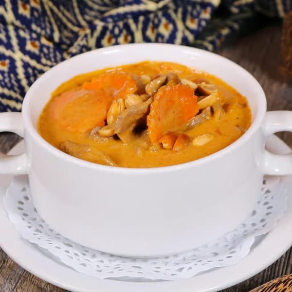 A white bowl of Thai red curry with carrots, mushrooms, and peanuts on a white doily.